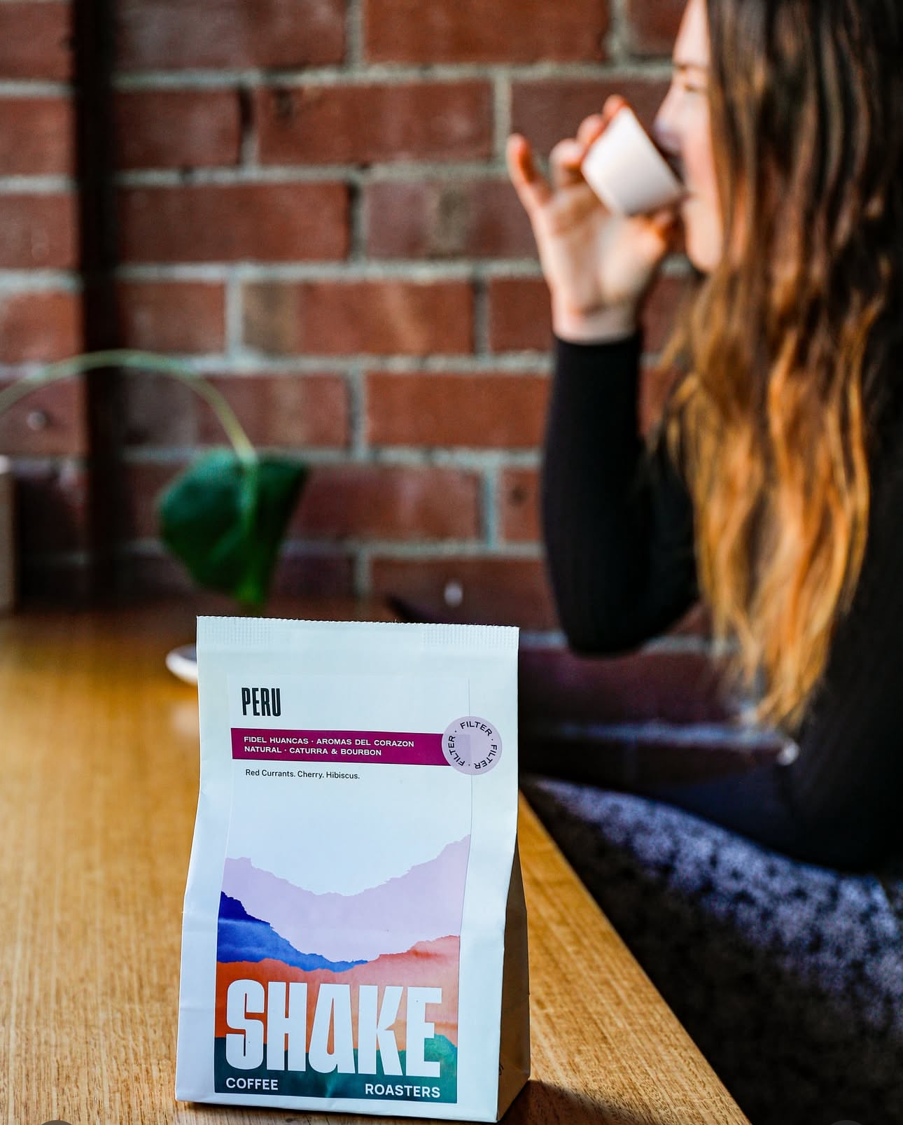 Person holding a coffee cup with a 'Shake' product packaging on a table.